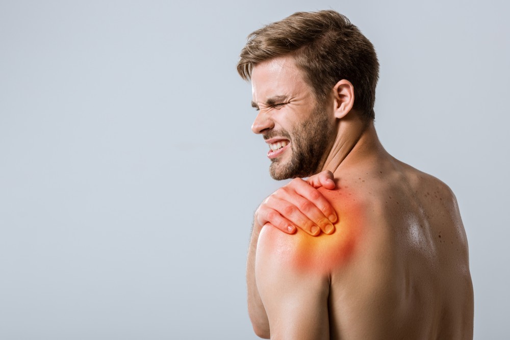 Man grimacing and squeezing his shoulder, which appears to be painful and inflamed.