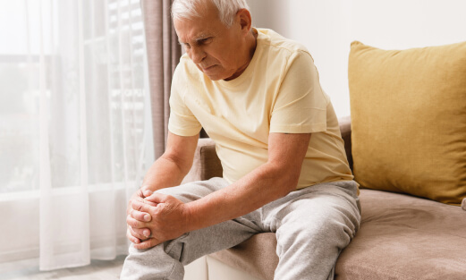 Elderly man leaning forward and holding his knee in pain.