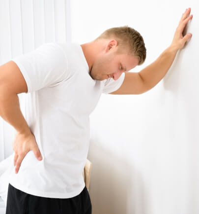 Man leaning against a wall while holding his lower back in pain.