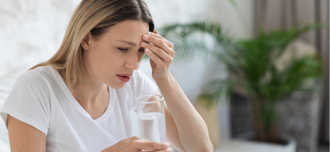 Woman holding glass of cool water while experiencing a headache.