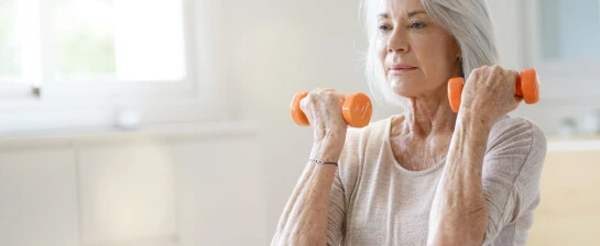 Physio Physique - Elderly woman confidently lifting hand weights.